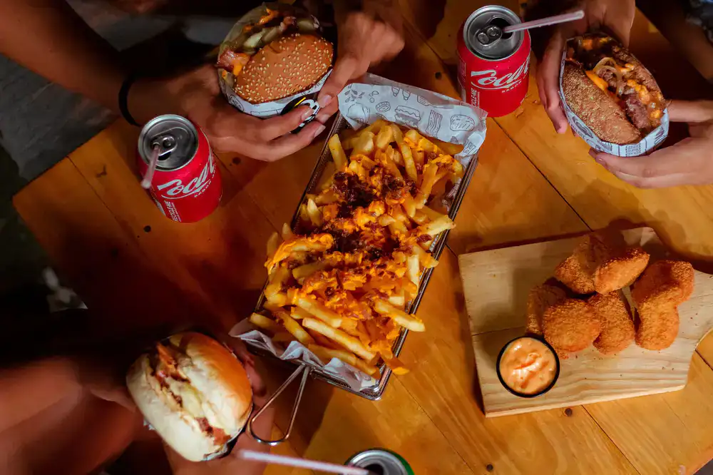 A spread of burgers, fries, and drinks at a gaming setup